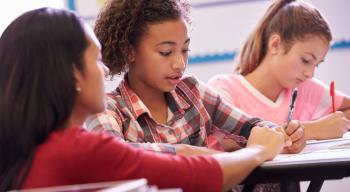 Children with pencils at desks in classroom